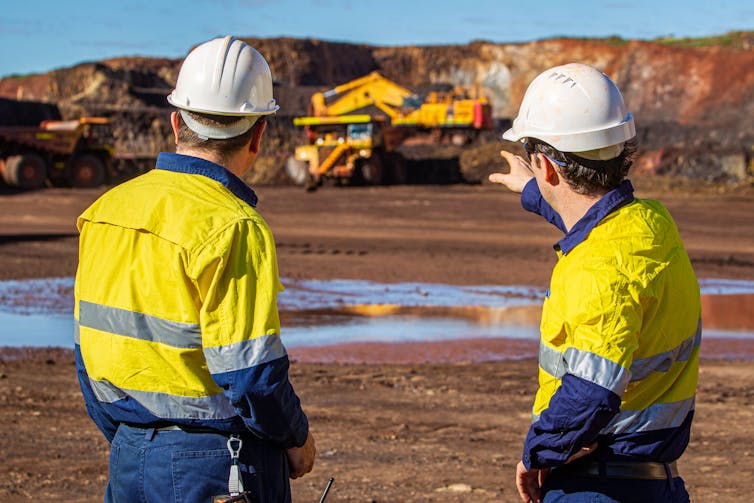 Two male miners standing in front of a mine pit and truck.