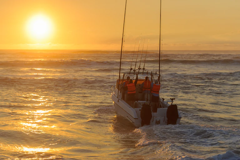 A photograph of a small boat heading out to sea as the sun rises