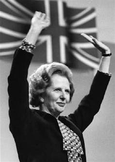Black and white photo of Margaret Thatcher with her hands raised in front of a union flag.