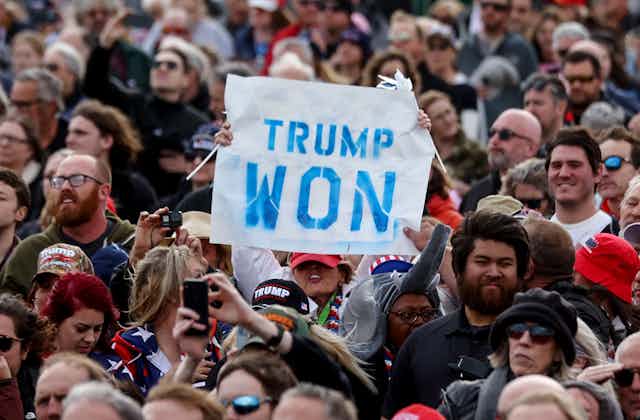 Una persona sostiene un cartel de "Trump ganó" en medio de una multitud