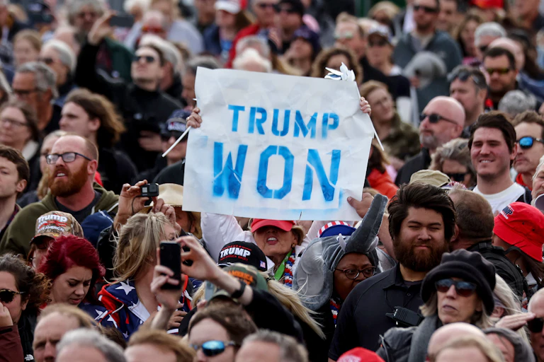 Una persona sostiene un cartel de "Trump ganó" en medio de una multitud