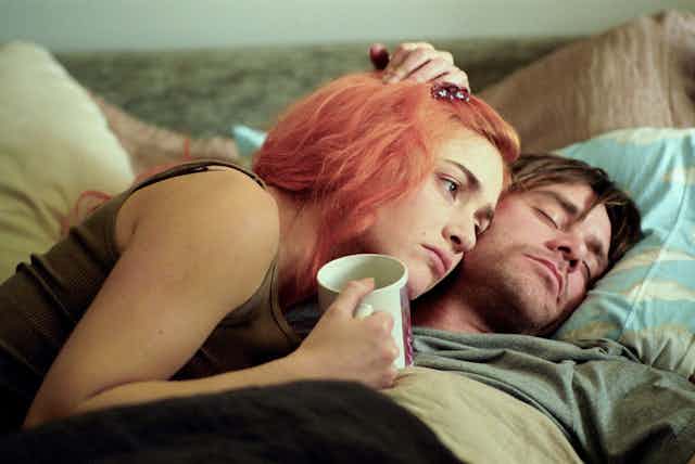 Kate Winslet with orange hair and Jim Carrey lay in bed.