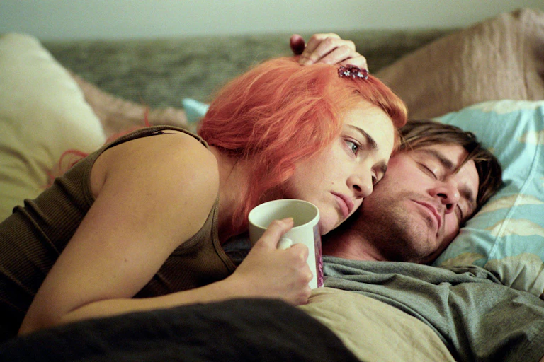 Kate Winslet with orange hair and Jim Carrey lay in bed.