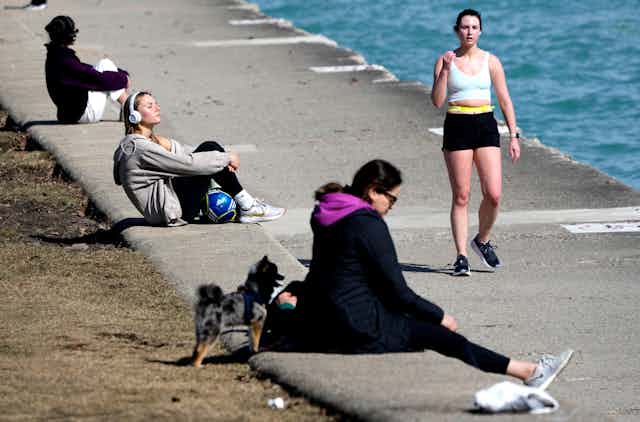A runner in shorts and tank top and people sitting along the shore of Lake Michigan.