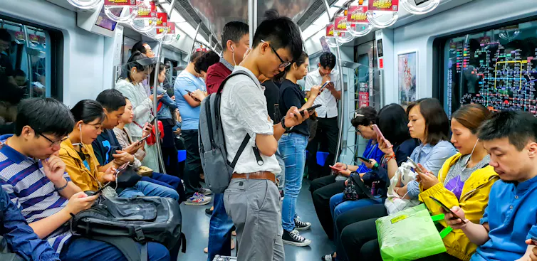 People hunched over their mobile phones ride on a train