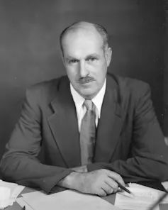 A white man dressed in a business suit looks into a camera without smiling.