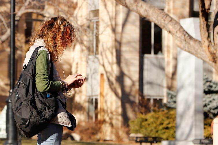 A woman with a backpack walks outside a building.
