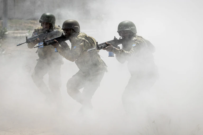 Three people holding guns while walking forward through a cloud of smoke