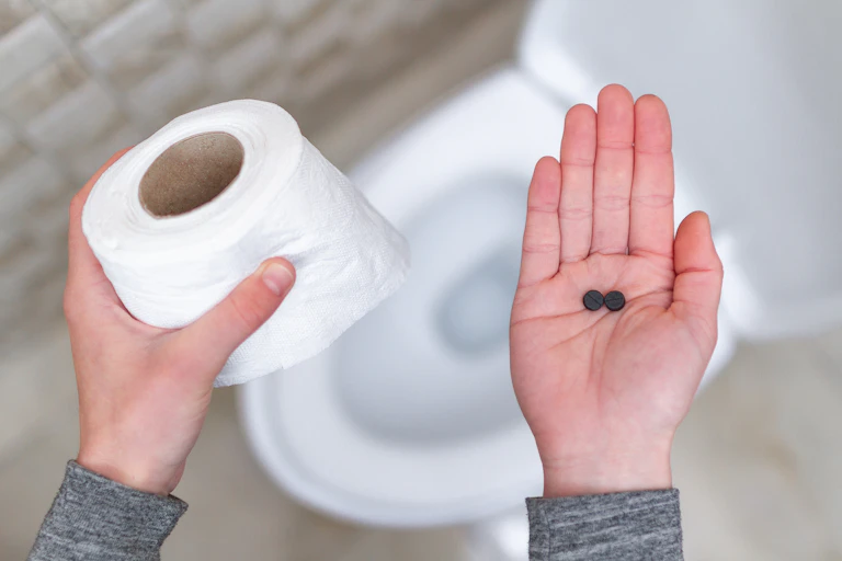 A person holds toilet roll in their left hand and two laxative pills in the palm of their right hand.