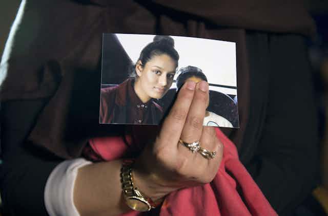 Close up of a woman's hand holding a photo of Shamima Begum as a schoolgirl. The woman's fingers are covering the face of another person in the photo.