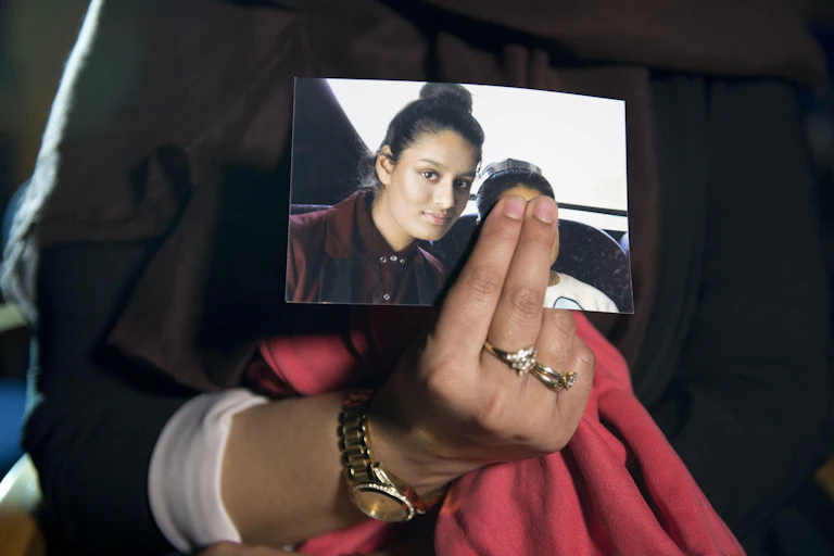 Close up of a woman's hand holding a photo of Shamima Begum as a schoolgirl. The woman's fingers are covering the face of another person in the photo.