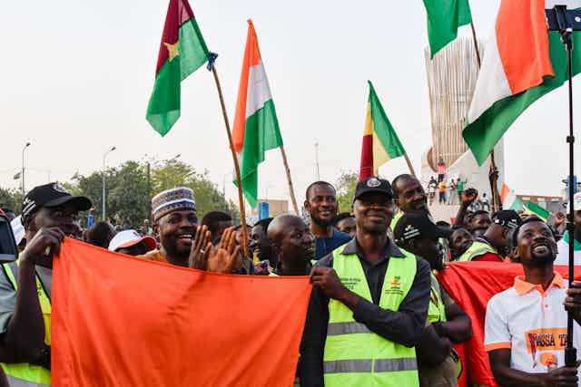 Personnes brandissant des drapeaux du Mali, du Niger et du Burkina Faso