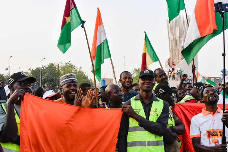 Personnes brandissant des drapeaux du Mali, du Niger et du Burkina Faso