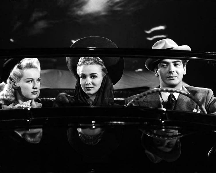 Dos mujeres y un hombre van en el asiento delantero de un descapotable.