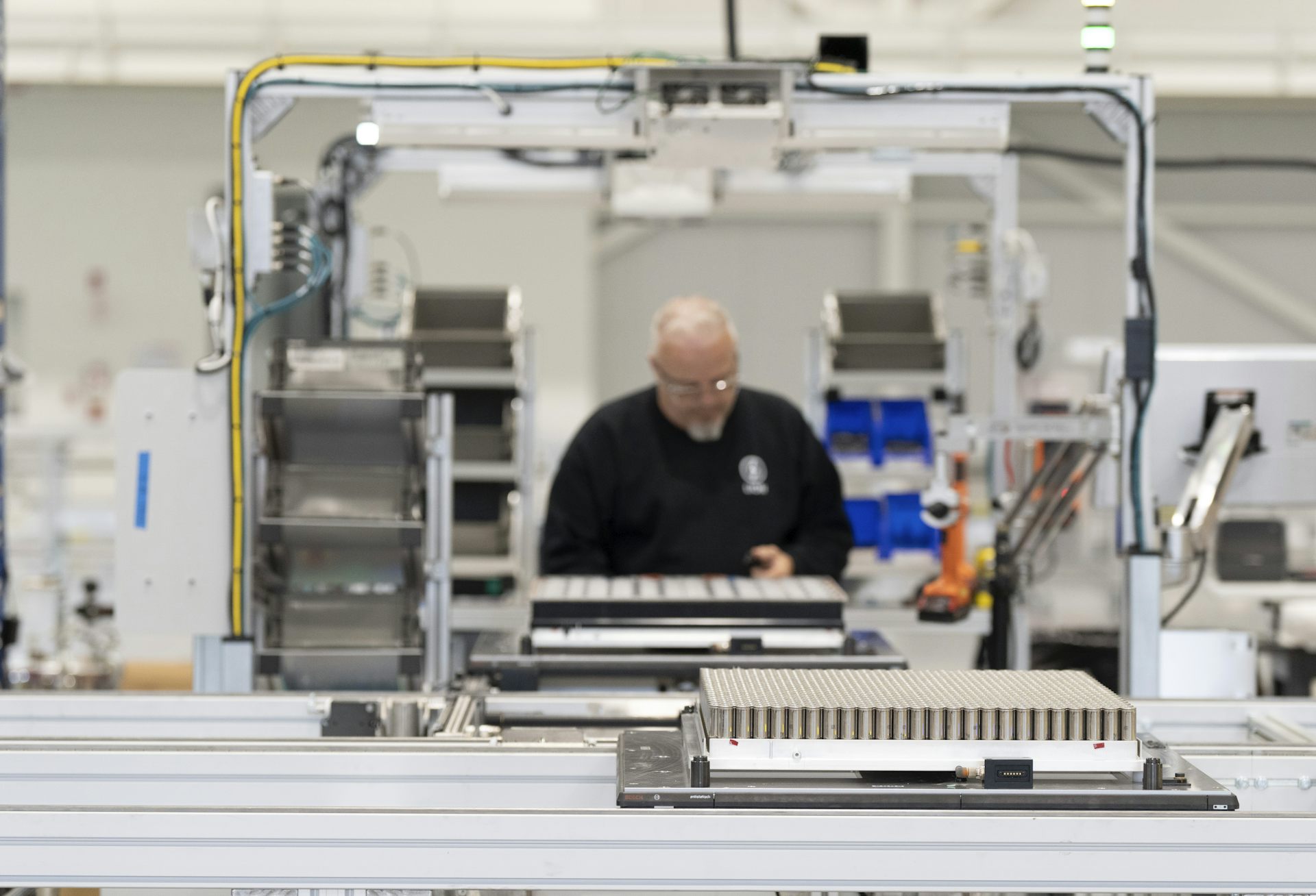 A man looks at a tray of batteries behind a conveyor belt.