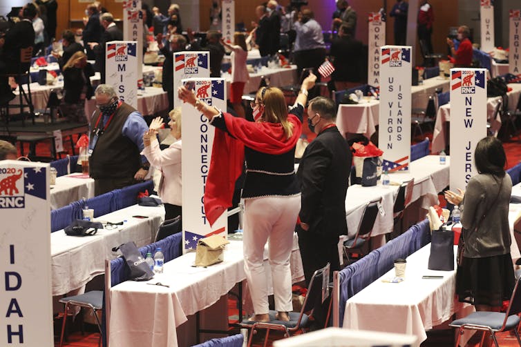 People stand at tables and raise their arms.