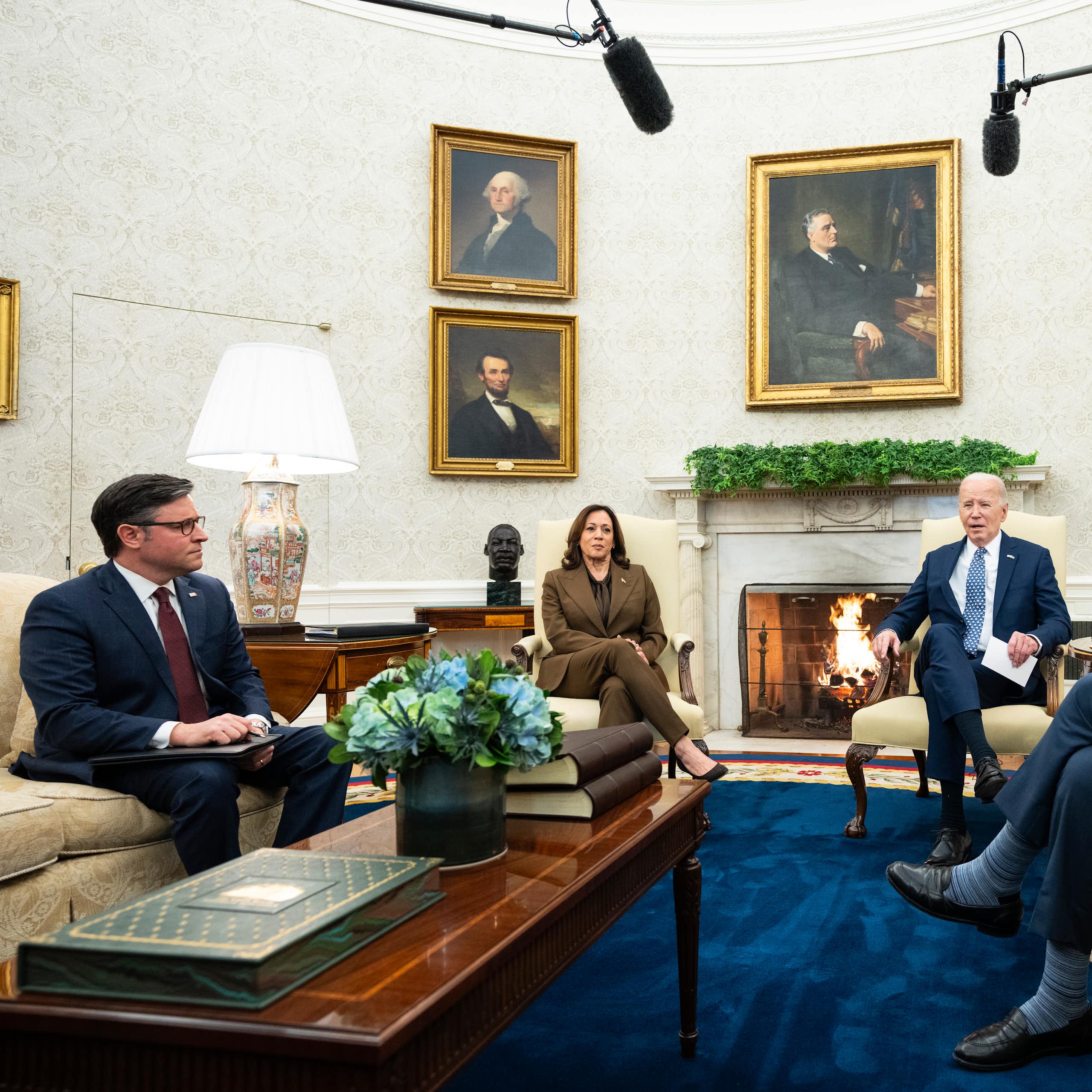 3 men and 1 woman are sitting on couches in an ornate room with presidential portraits on the wall and a fireplace