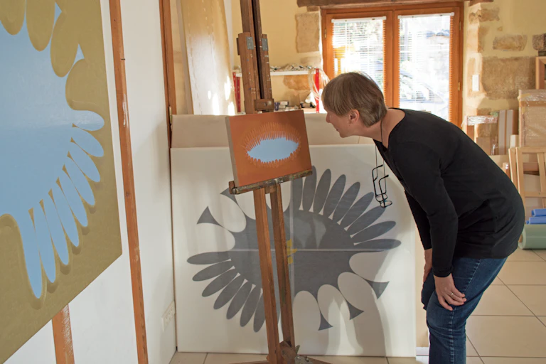 A middle-aged woman bending over to look at a painting she is working on.