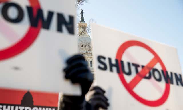 signs with the word 'shutdown' and a circle and cross through it are held up in front of capitol building