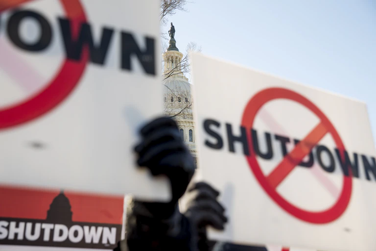 signs with the word 'shutdown' and a circle and cross through it are held up in front of capitol building