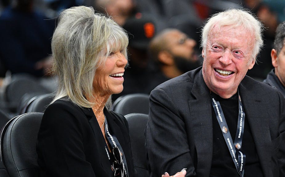 An older couple dressed all in black smile at a sporting event.