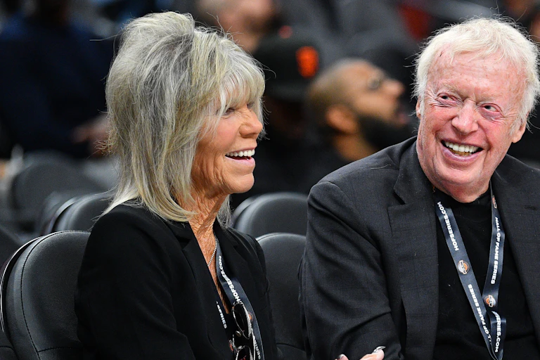 An older couple dressed all in black smile at a sporting event.
