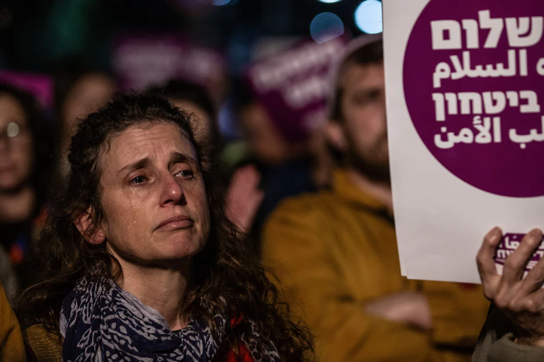 A brunette woman with a tear running down her face stands amid a crowd of people holding signs.