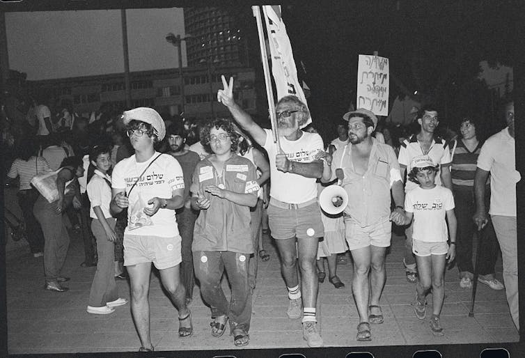 Four adults and a child walk together, leading a march with city buildings in the background, in a black and white photo.