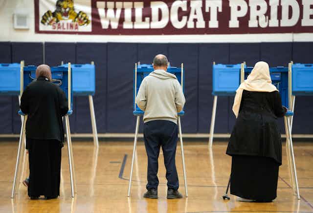 Three voters appear from the back at voting booths.