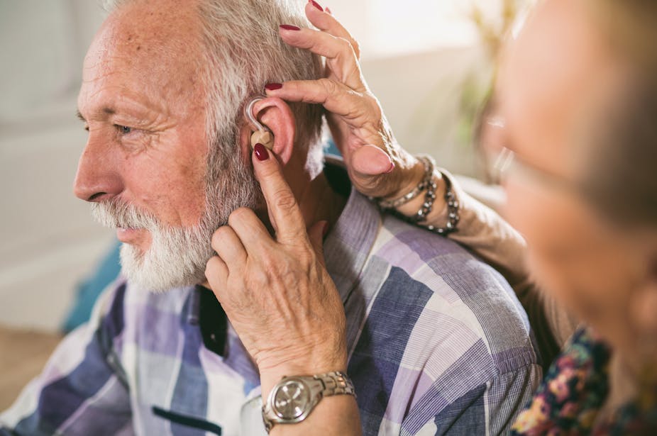 A woman helps fasten a hearing aid onto a senior man's ear.