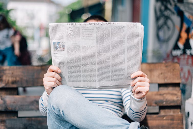 A person reading a newspaper on a bench.