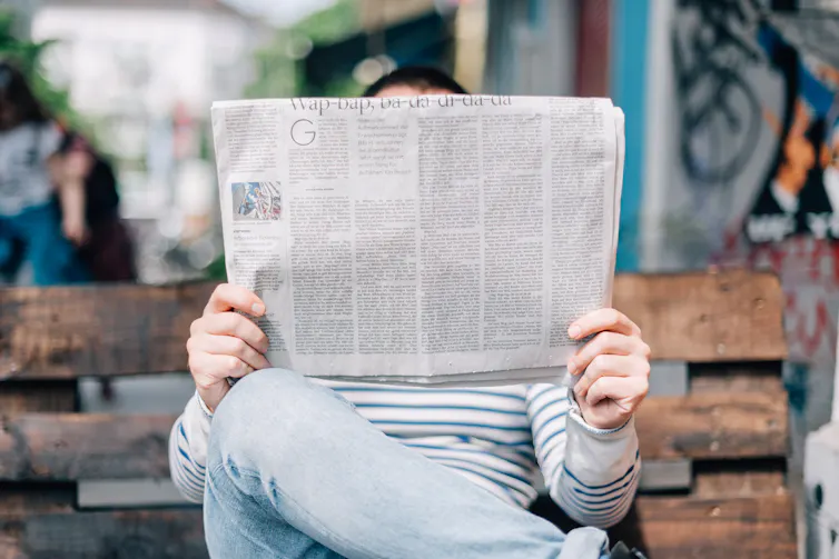 A person reading a newspaper on a bench.
