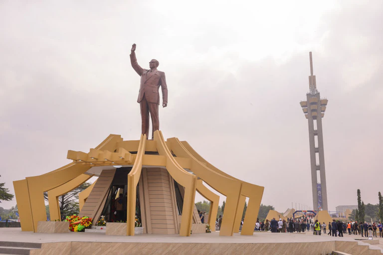 A statue with an arm raised, behind it a tower.