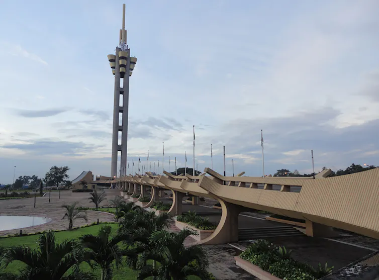 A concrete pathway with curved sides leads to a large tower with a flower-like top.
