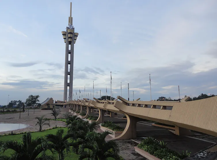 A concrete pathway with curved sides leads to a large tower with a flower-like top.