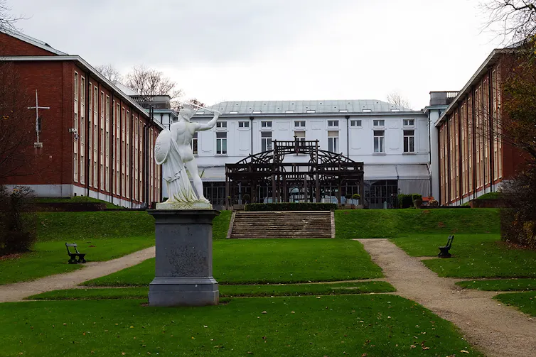 An old building with a statue in the foreground, behind it a wooden structure that is a curved frame.