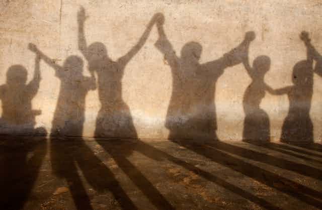 The shadows of children are seen on a wall as they hold each other's hands aloft