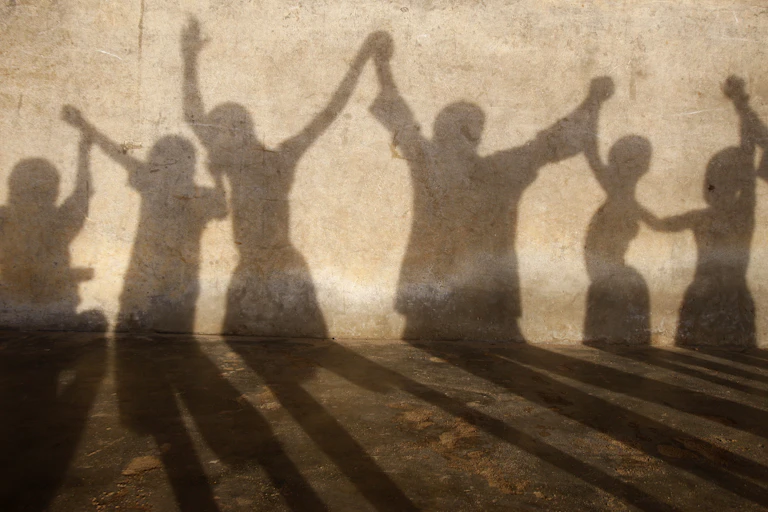 The shadows of children are seen on a wall as they hold each other's hands aloft