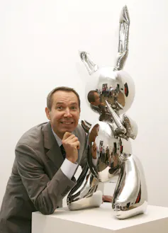 A smiling man with a metal sculpture of a rabbit on a plinth.