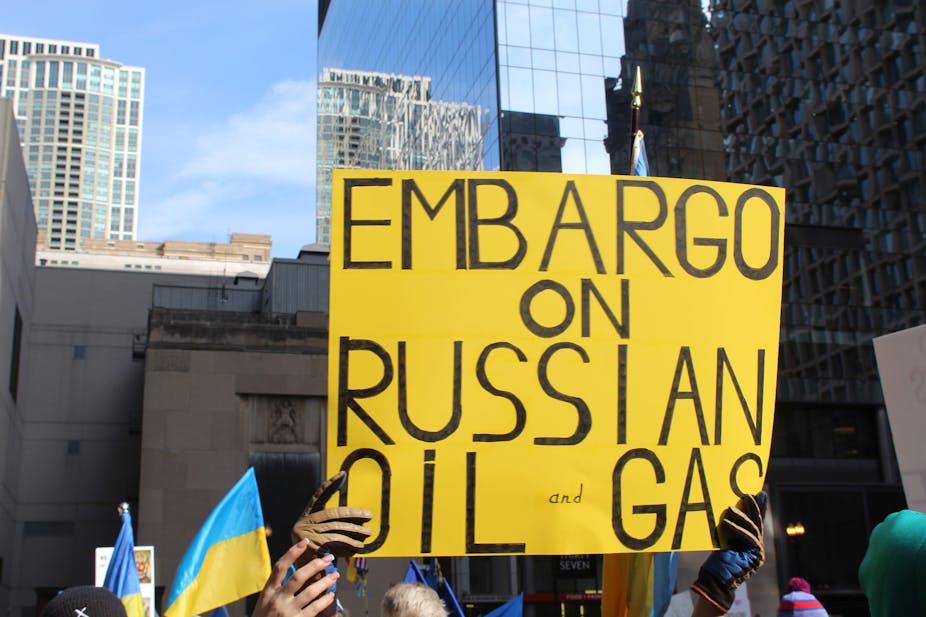 Two people hold a yellow sign saying: embargo on Russian oil and gas.