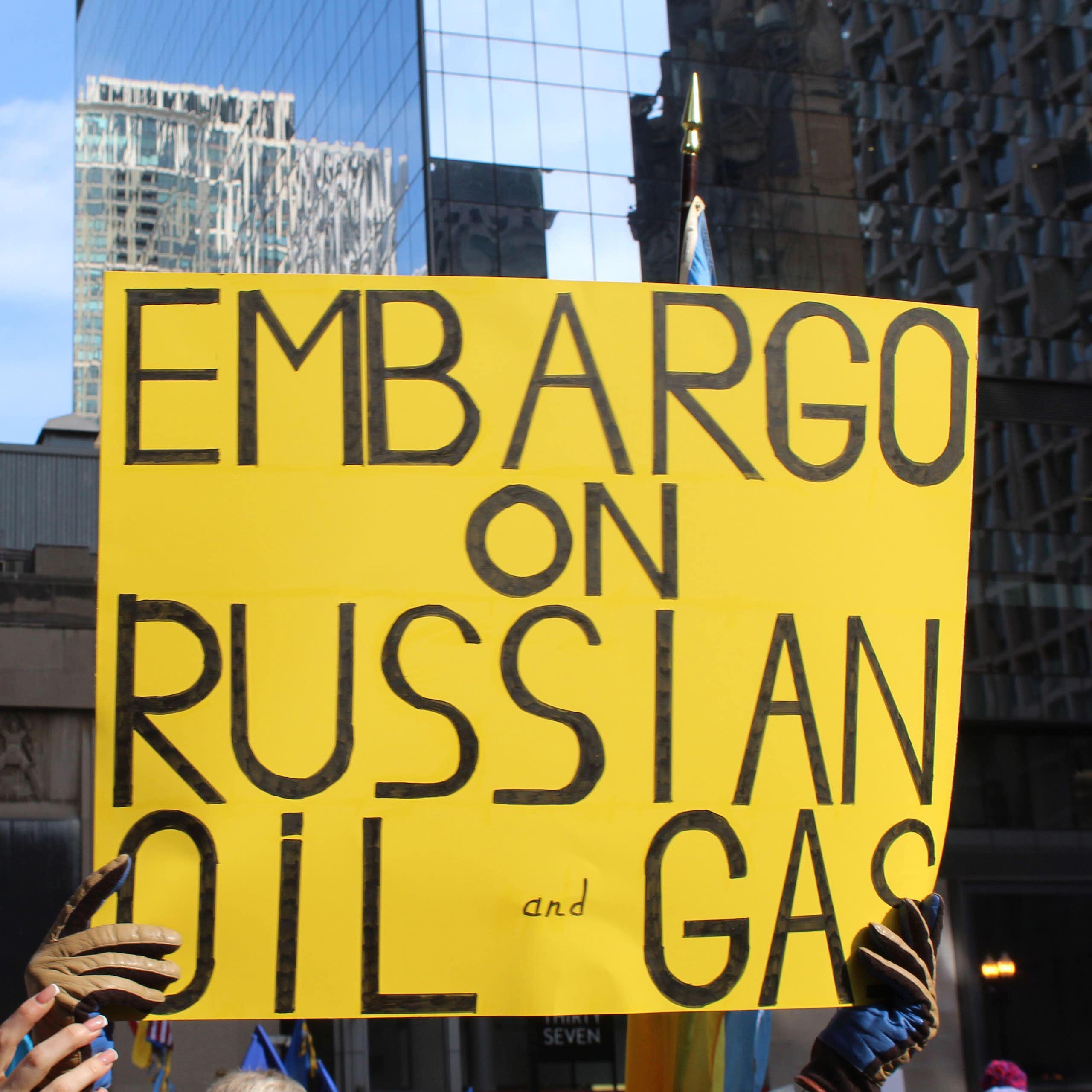 Two people hold a yellow sign saying: embargo on Russian oil and gas.
