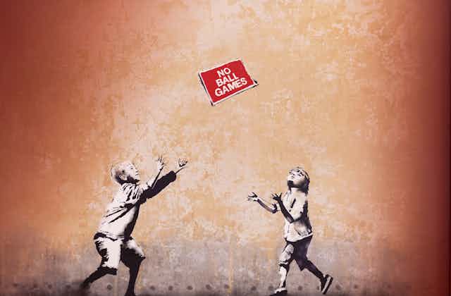 A Banksy mural showing two children throwing a 'No ball games' sign to each other