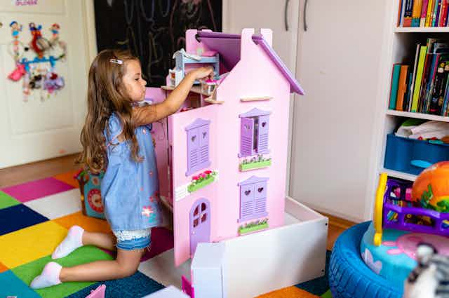 A girl rearranges furniture in a purple dollhouse.