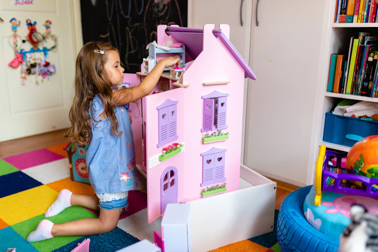 A girl rearranges furniture in a purple dollhouse.
