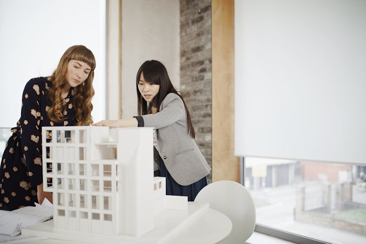 Two women look at a miniature model of a building.
