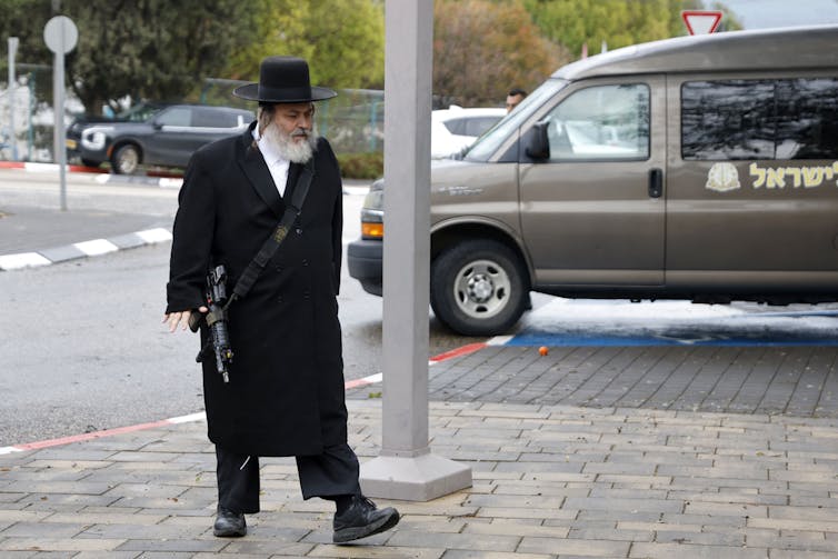 An man dressed in ultra-Orthodox Jewish clothes carries a weapon.