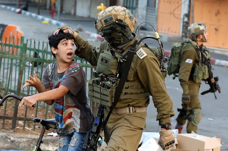 An IDF soldier pulls the hair of a young Palestinian boy while arresting him.