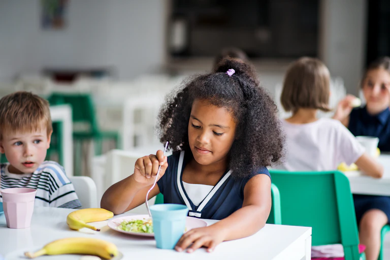 A child eats food off a plate in a classroom