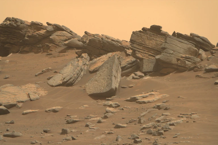 A photograph of the Martian surface shows a tangerine-colored sky and massive rocks sitting on rust-colored soil.