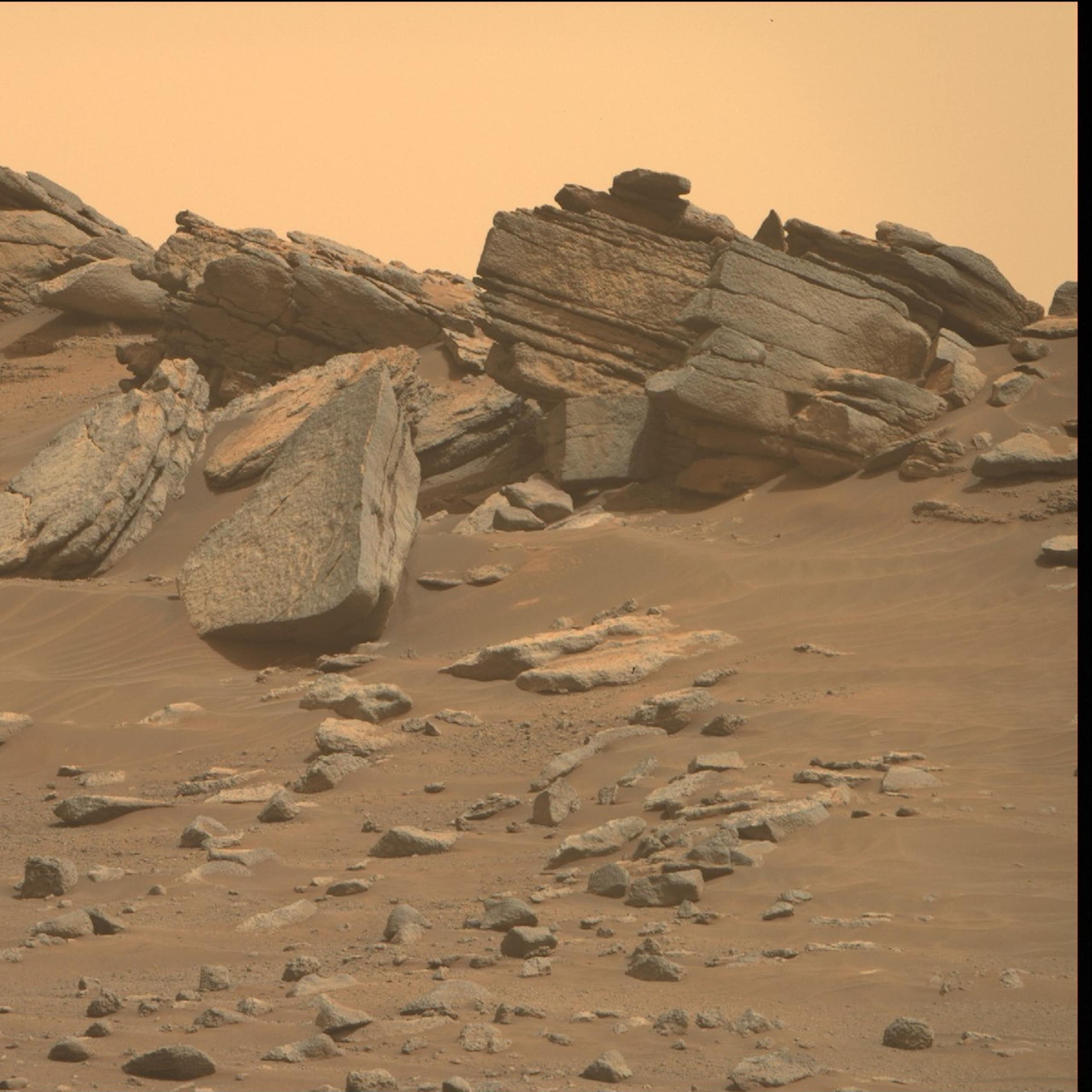 A photograph of the Martian surface shows a tangerine-colored sky and massive rocks sitting on rust-colored soil.
